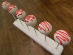 six cake pops with red icing sitting on top of a white stand in the middle of a wood floor