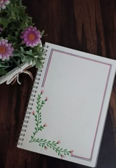 an open notebook with flowers on it sitting next to a potted plant in the background