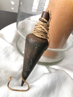 an old metal object with rope wrapped around it sitting next to a glass vase filled with liquid