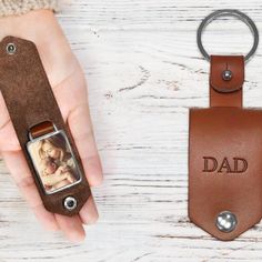 a hand holding a brown leather keychain with a photo on it and the word dad engraved on it