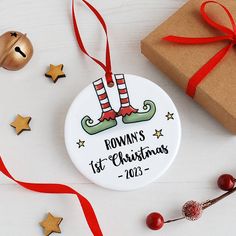 personalized christmas ornament with elf legs and red ribbon on white table next to presents