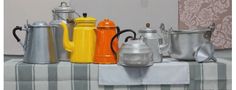 an assortment of coffee pots and kettles are on a table with a striped cloth