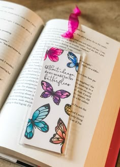 an open book with butterflies on it and a pink ribbon attached to the cover, sitting on a table