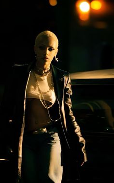 a woman walking down the street at night with her shirt off and jacket open, wearing all black