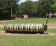 a large black and yellow striped object in the middle of a park with trees behind it