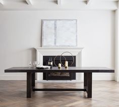 a dining table with candles on it in front of a fire place and paintings above