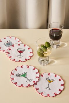 three coasters on a table with wine glasses and olives in front of them