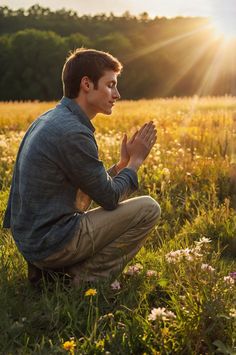 a young man kneeling in a field with his hands clasped to the ground while praying