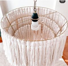 a light that is on top of a white lamp shade with tassels hanging from it