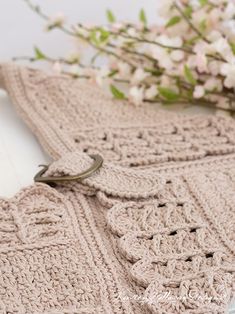 there is a crocheted shawl on the table next to a vase with flowers