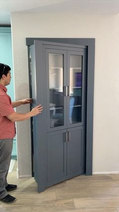 a man standing in front of a tall cabinet with glass doors on both sides and his hand reaching for the door