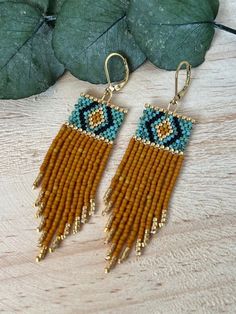 two pairs of beaded earrings sitting on top of a wooden table next to a leaf