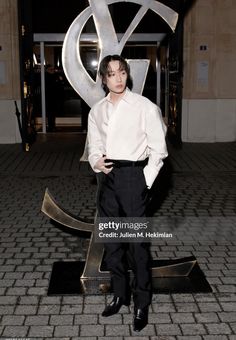 a man standing in front of a large metal sculpture with the letter s on it