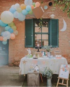 an outdoor party with balloons and decorations on the table, near a brick building that has green shutters