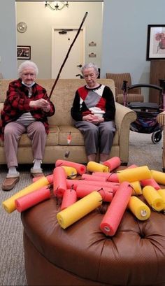 two elderly people sitting on a couch with many dynamites in front of them and one is holding a fishing pole