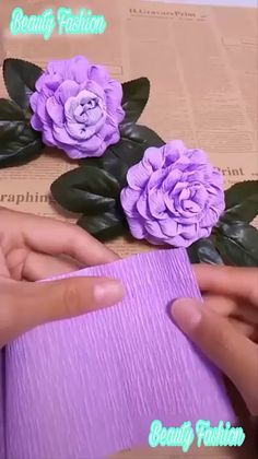 two hands are holding purple paper and some flowers