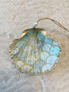 a blue and white shell on sand with a beaded necklace hanging from it's side