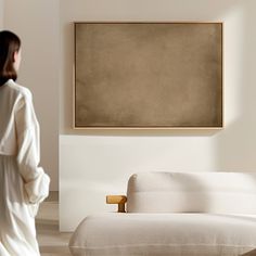 a woman standing in front of a white couch with a brown painting on the wall