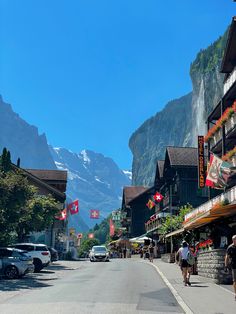 people are walking down the street in front of some buildings with mountains in the background