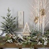 a fireplace mantel decorated with christmas trees and evergreens, pine cones and white berries