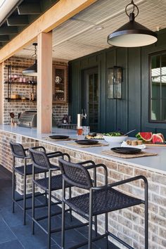 an outdoor bar with black chairs and plates on it, next to a brick wall