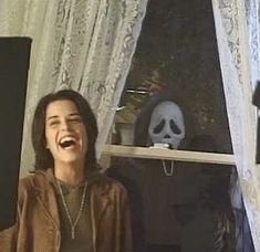 a woman laughing while standing in front of a window with a skeleton head on it