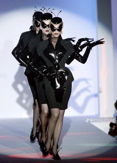 two women in black catsuits walking down a runway