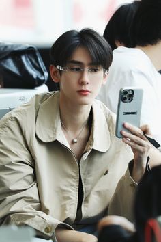 a young man wearing glasses is looking at his cell phone while sitting in an airport