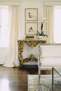 a living room filled with furniture and paintings on the wall next to a window covered in curtains