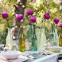 there are many vases with flowers in them on the dining room table set for dinner