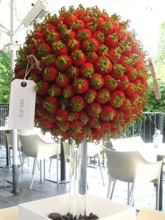 a large bushel of strawberries on display in a room with tables and chairs