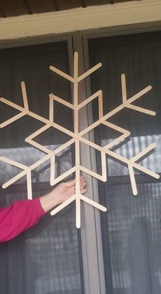 a woman standing next to a window with a wooden snowflake hanging from it's side