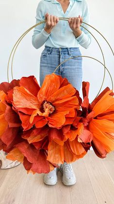 a woman standing in front of an orange flower arrangement with hoop holding it up to her face