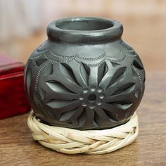 a black vase sitting on top of a wooden table next to a red box and rope