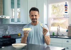 a man holding a bowl and spoon while standing in front of a kitchen counter top