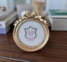 a small gold frame with a pink flower on it sitting on a wooden table next to a vase