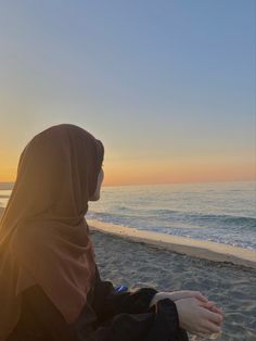 a woman sitting on top of a sandy beach next to the ocean at sunset or dawn