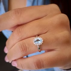 a close up of a person's hand wearing a ring with an aqua blue topazte