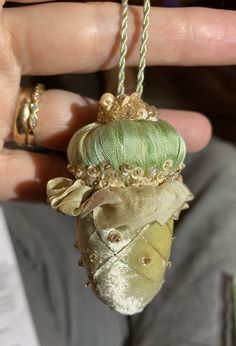 a person is holding a green ornament in their left hand and gold jewelry on the other hand