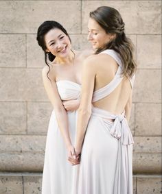 two women standing next to each other in front of a stone wall and holding hands