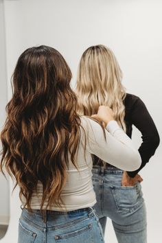 two women standing in front of a mirror with their backs to the camera and one is wearing jeans