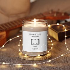 a lit candle sitting on top of a wooden table next to a guitar and some string lights