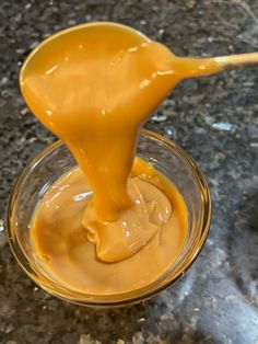 a spoon full of caramel sauce sitting on top of a glass bowl filled with liquid