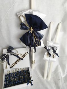 two white candles with blue ribbons and some other items in the box on a bed