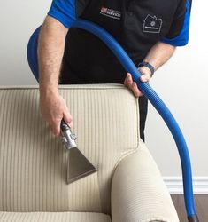 a man is holding a vacuum and cleaning the back of a couch with a blue hose