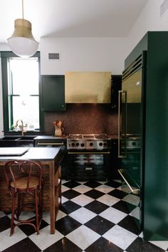 a black and white checkered floor in a kitchen with green cabinets, an island table and chairs