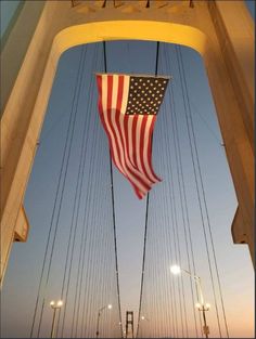 an american flag hanging from the side of a suspension bridge with street lights in the background