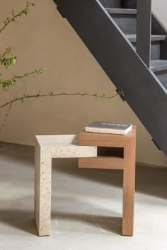 a small table with a book on it in front of a stair case next to a plant