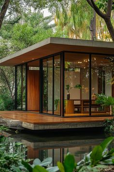 a house that is sitting in the middle of some water with trees and plants around it