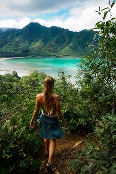 a woman is walking up a trail towards the water and mountains in the tropical area